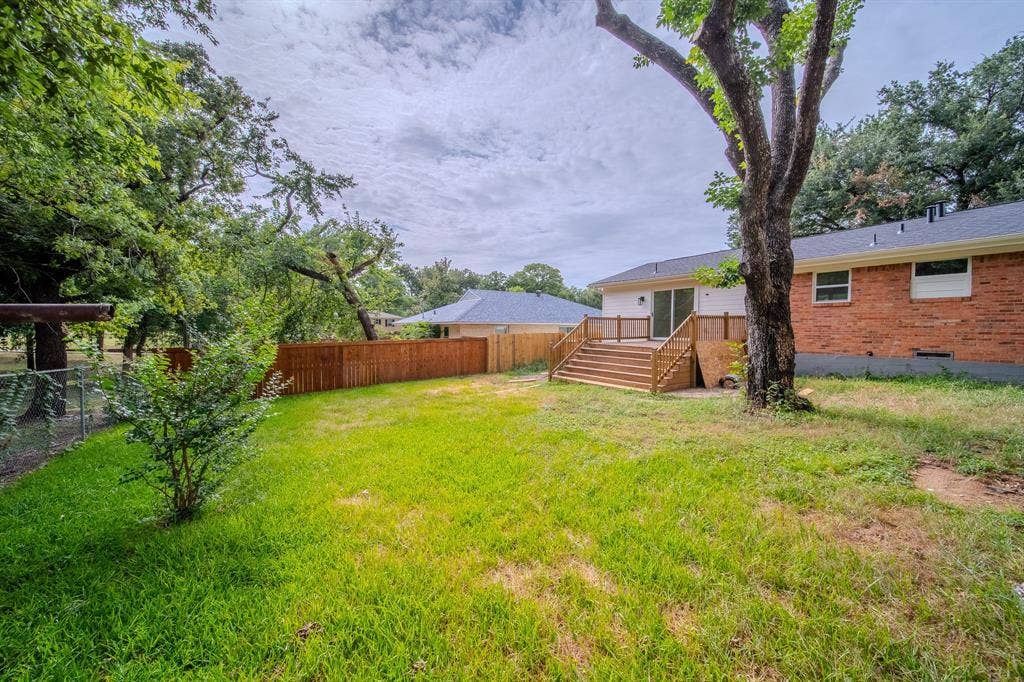 Spacious backyard with a wood privacy fence, chain-link fence, mature trees, and a multi-level wood deck featuring white railings and a sliding glass door