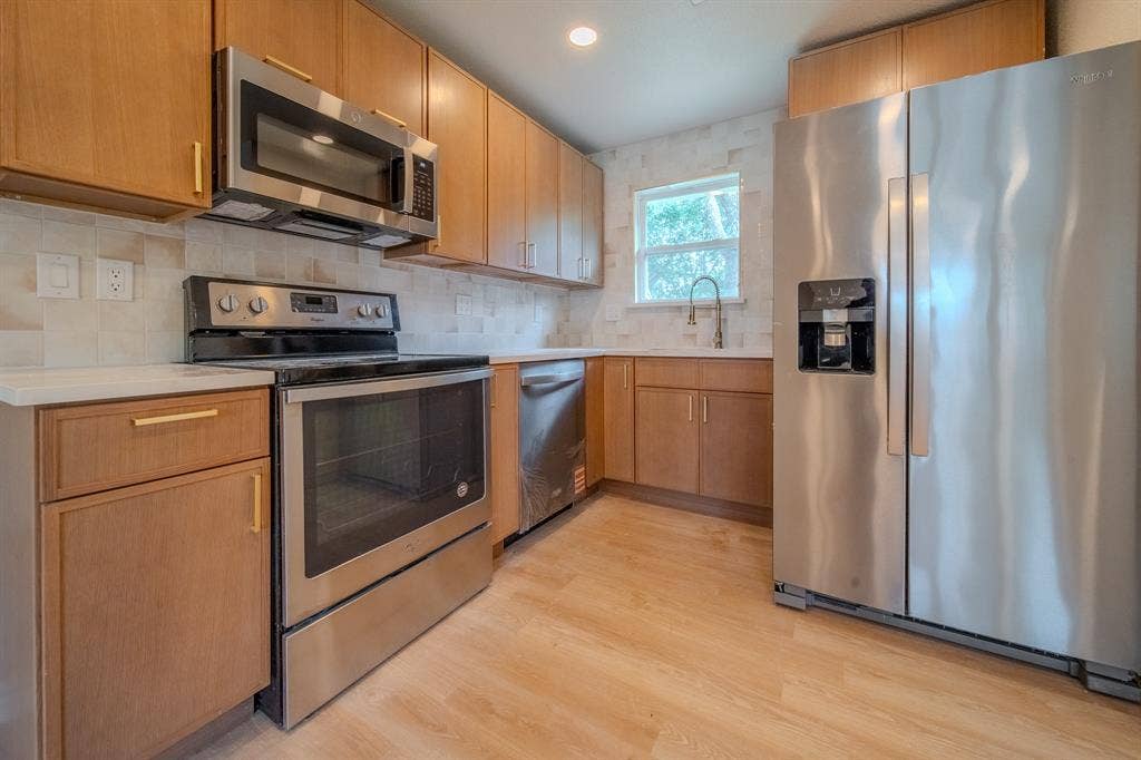 Modern kitchen featuring wood-finish cabinetry, stainless steel appliances, white countertops, a tiled backsplash, and wood-finish flooring