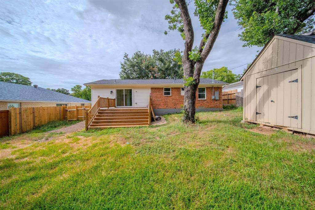 Expansive backyard featuring a multi-level wood deck with railings, a sliding glass door entry to the home, a detached storage shed, a wood privacy fence, and mature trees