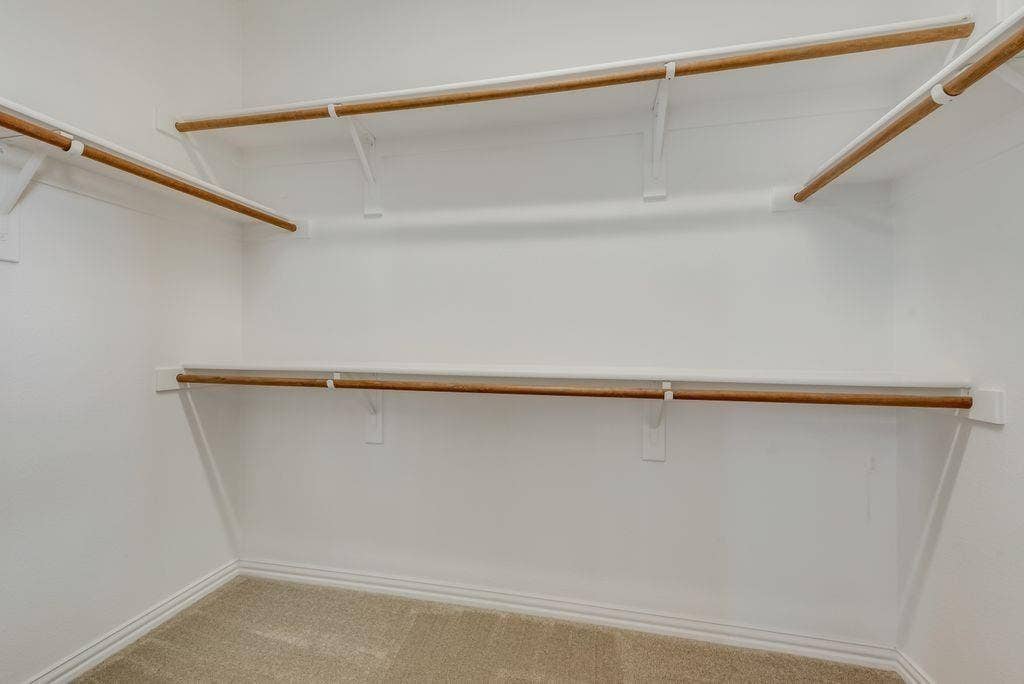 1709 Belton Drive, Prosper, TX 75078 Walk-in closet featuring light-colored carpeting, white baseboards, and built-in white shelving with wooden hanging rods