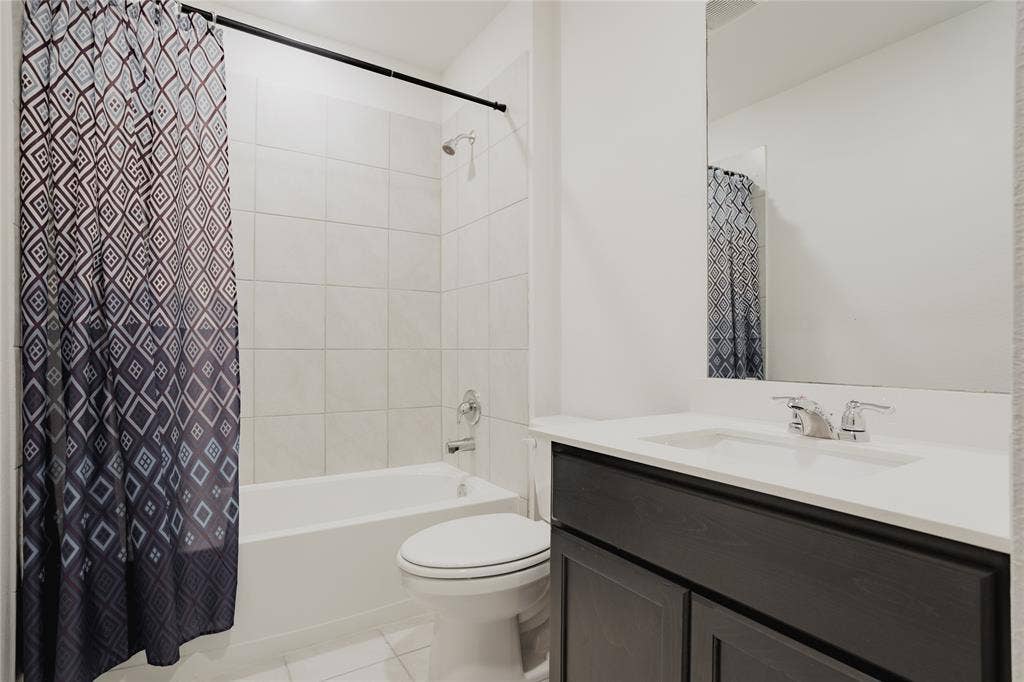 2904 Goodrich Street, Royse City, TX 75189 Bathroom featuring a white bathtub, ceramic tile surround, and a dark wood-finish vanity with an integrated sink and chrome fixtures
