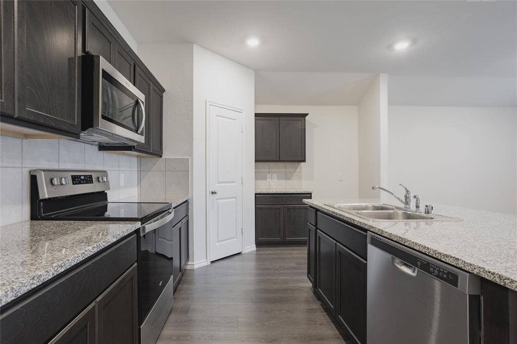 2904 Goodrich Street, Royse City, TX 75189 Kitchen with dark wood cabinetry, light speckled countertops, stainless steel appliances, and wood-finish flooring