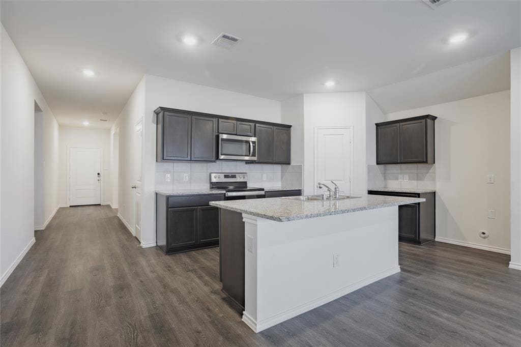 2904 Goodrich Street, Royse City, TX 75189 Modern kitchen featuring dark wood-finish cabinetry, stainless steel appliances, a white tile backsplash, and a central island with a light-colored countertop
