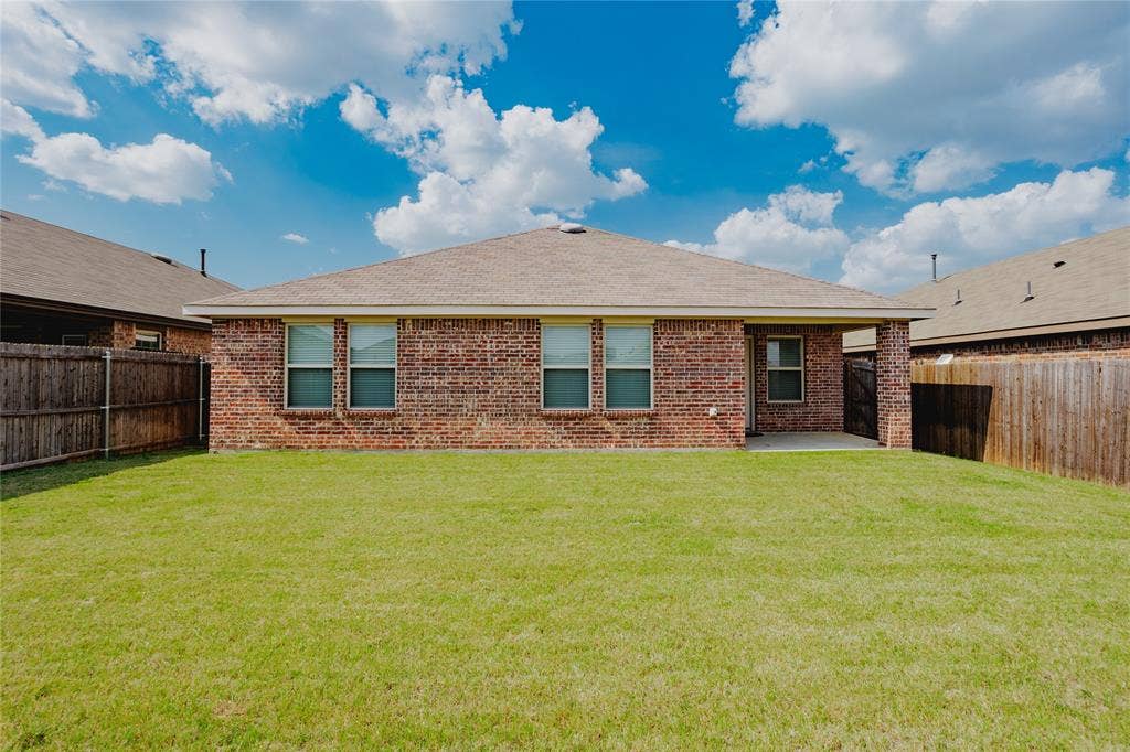 2904 Goodrich Street, Royse City, TX 75189 Expansive backyard featuring a manicured lawn, full brick exterior, multiple windows with white trim, a covered patio, and a privacy fence
