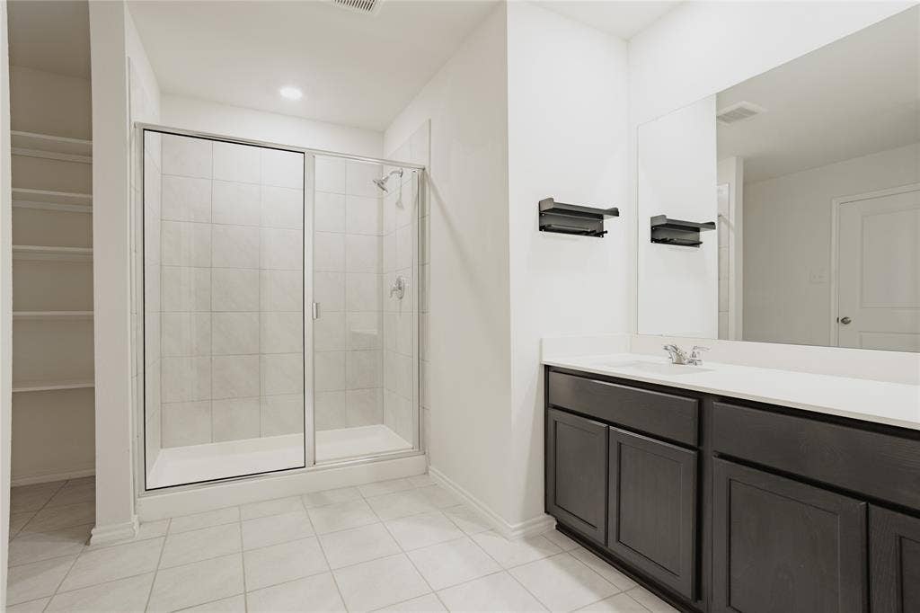 2904 Goodrich Street, Royse City, TX 75189 Bathroom featuring a glass-enclosed shower with tiled walls, a dark wood-finish vanity with a light-colored countertop, and a built-in shelving unit