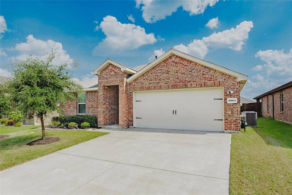 2904 Goodrich Street, Royse City, TX 75189 Brick exterior with a peaked roofline, an attached two-car garage, a concrete driveway, and a manicured lawn with established landscaping
