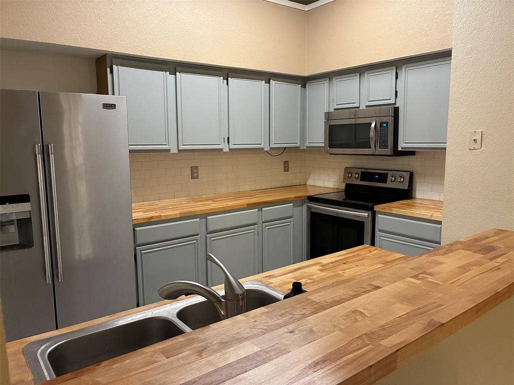 2062 Bronco Lane, Keller, TX 76248 Kitchen featuring light blue cabinetry, wood-finish countertops, stainless steel appliances, and a subway tile backsplash