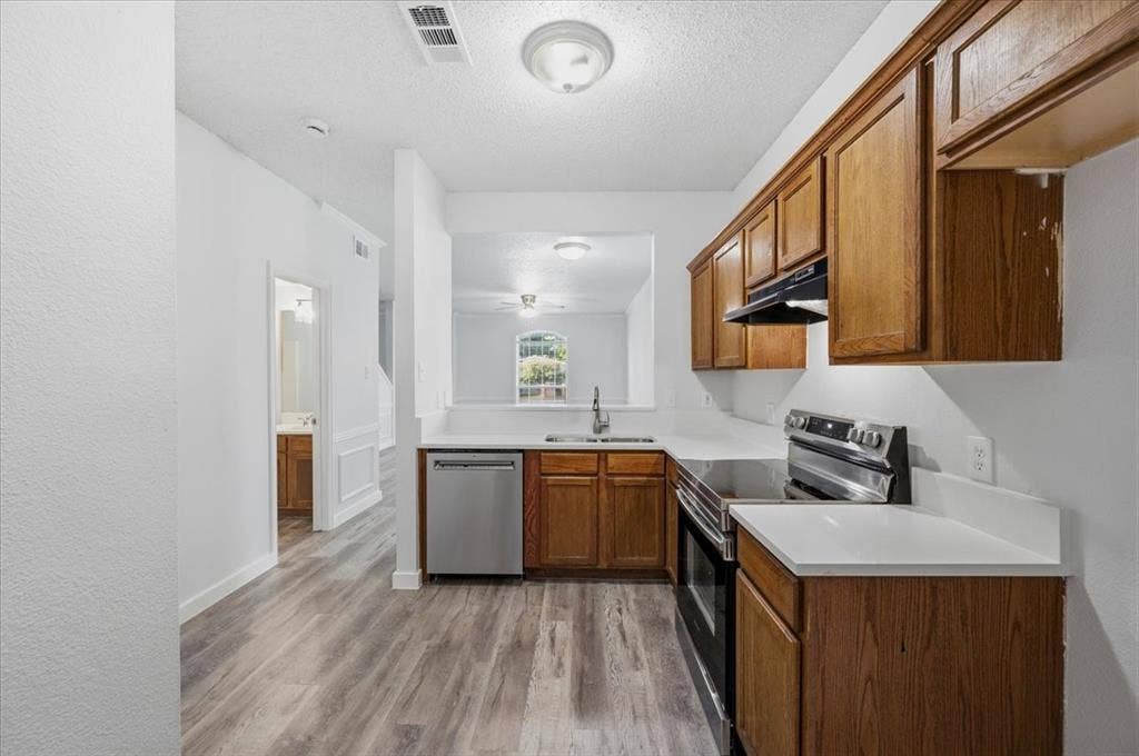 2122 W E Roberts Drive, Grand Prairie, TX 75051 Kitchen featuring wood-finish cabinetry, stainless steel appliances, a stainless steel sink with a gooseneck faucet, and light-toned countertops