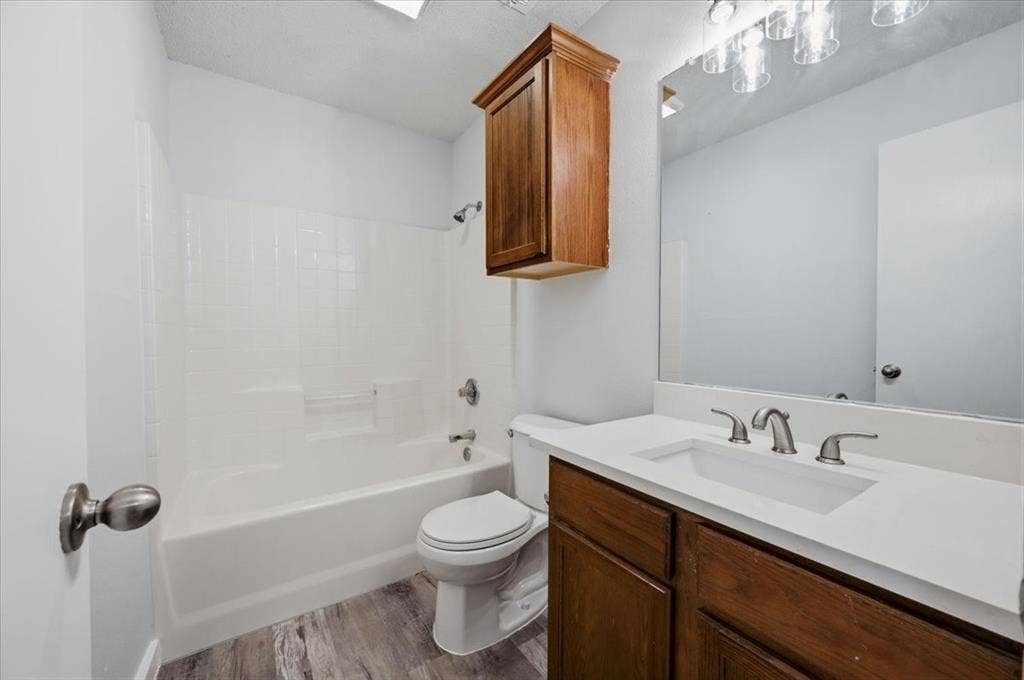 2122 W E Roberts Drive, Grand Prairie, TX 75051 Bathroom featuring a white bathtub with an integrated shower, a white vanity countertop with an undermount sink, a wood-finish vanity cabinet, a wall-mounted mirror with overhead lighting, and wood-finish flooring