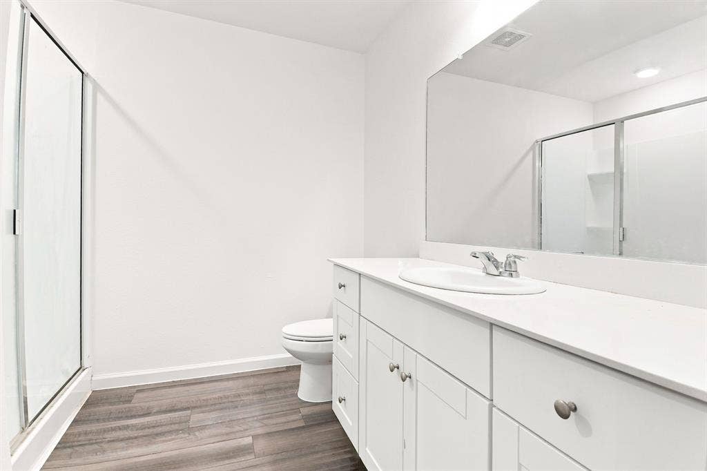 6520 Calico Lane, Forney, TX 75126 Bathroom featuring a spacious vanity with white cabinetry and an integrated sink, a large wall-mounted mirror, a glass-enclosed shower, and wood-finish flooring