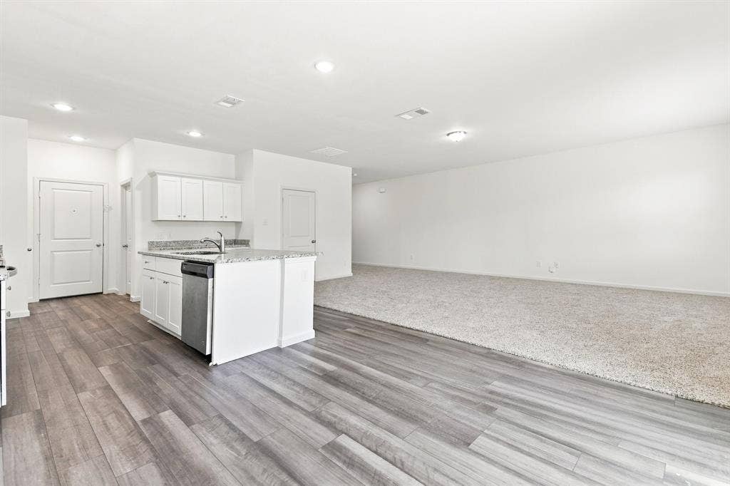 6520 Calico Lane, Forney, TX 75126 Open-concept living space featuring wood-finish flooring, white cabinetry, a kitchen island with a built-in sink and dishwasher, recessed lighting, and light-colored carpeting