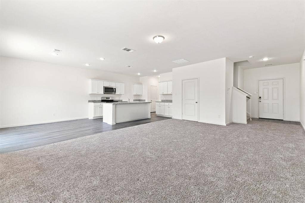 6520 Calico Lane, Forney, TX 75126 Spacious living area featuring light gray carpeting and a kitchen with white cabinetry, stainless steel microwave, and an island with a countertop