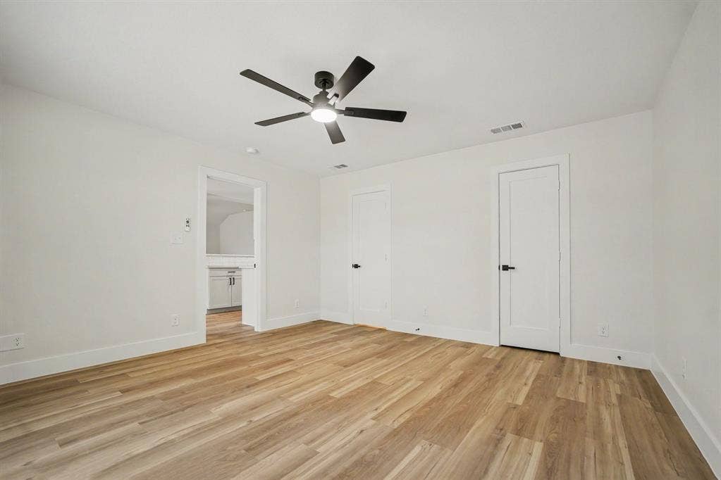 Spacious primary bedroom featuring wood-finish flooring, white walls, and a contemporary ceiling fan