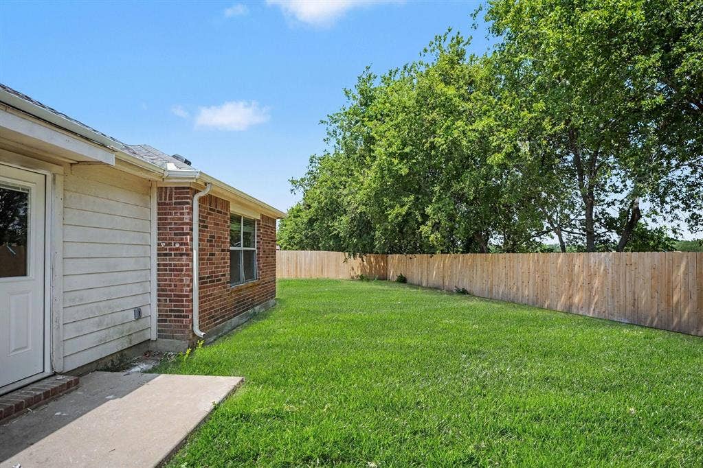 Spacious backyard featuring a manicured lawn, mature tree line providing natural privacy screening, and wooden perimeter fencing