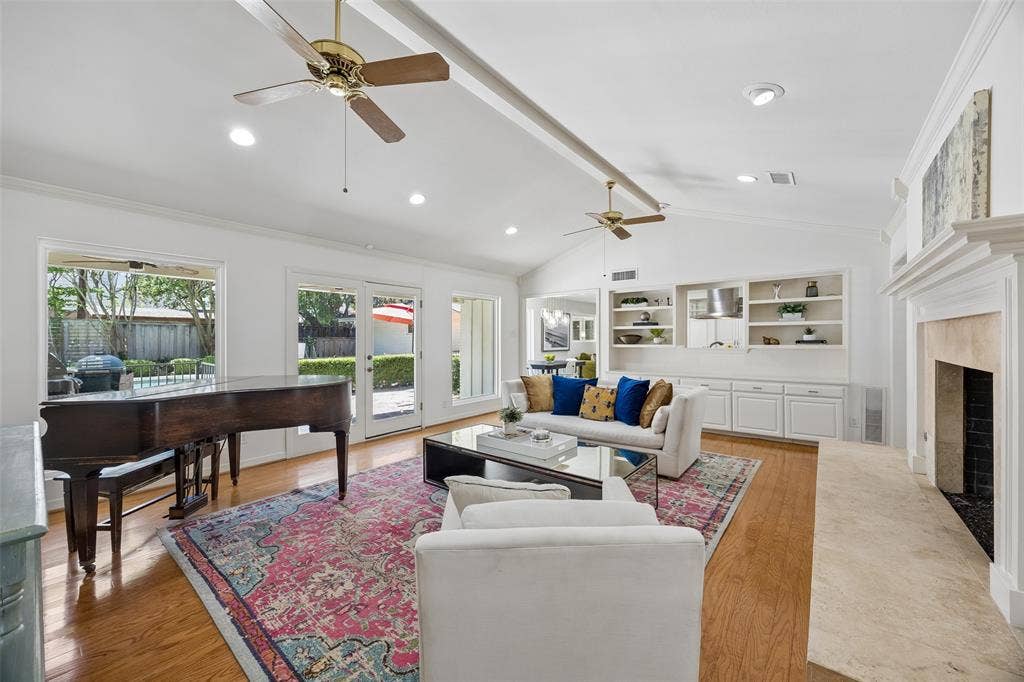 4110 Shady Hill Drive, Dallas, TX 75229 A wider view of the living room showcases the vaulted ceiling, fireplace, custom built-ins, wood floors, and seamless connection to the kitchen, backyard and pool.