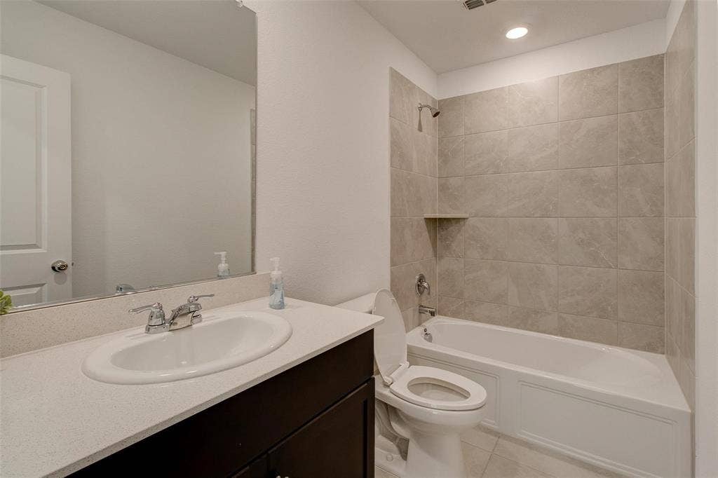 6005 Determine Lane, Forney, TX 75126 Bathroom featuring a single vanity with a white countertop and dark wood cabinetry, an undermount sink with chrome fixtures, a full-width mirror, and a bathtub with light gray tiled surround and built-in shelf