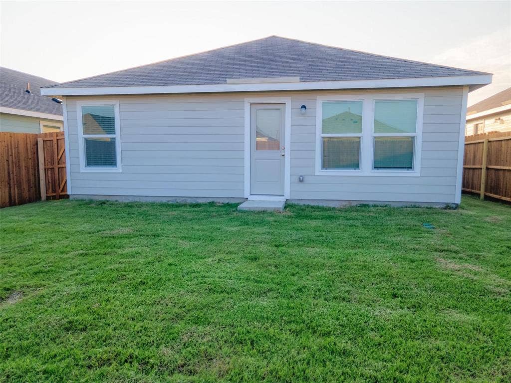 6005 Determine Lane, Forney, TX 75126 Spacious backyard with a vibrant green lawn, light-colored siding, multiple windows, a rear entry door, and perimeter fencing