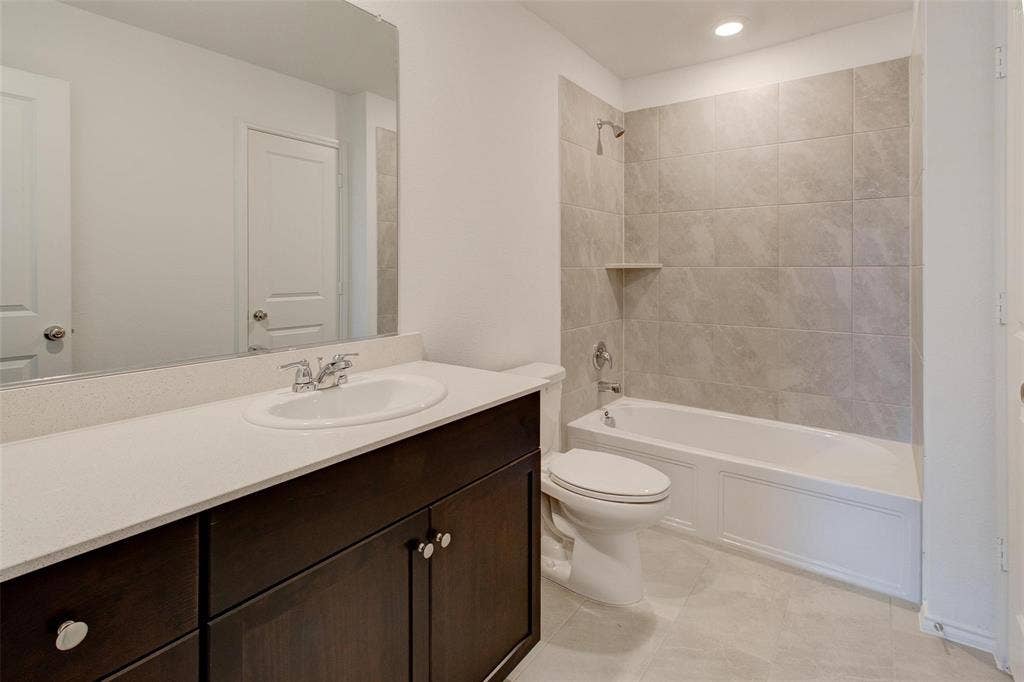 6005 Determine Lane, Forney, TX 75126 Bathroom featuring a dark wood vanity with a white countertop and undermount sink, a white tub and shower combination with light-toned tile surround, and recessed lighting