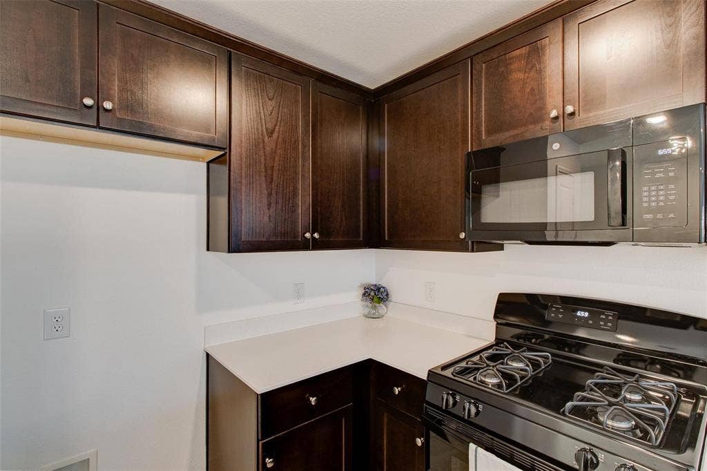 6005 Determine Lane, Forney, TX 75126 Kitchen featuring dark wood-finish cabinetry, light countertops, an over-the-range microwave, and a black gas range