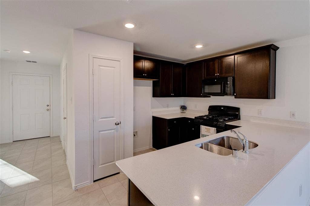 6005 Determine Lane, Forney, TX 75126 Kitchen featuring dark wood cabinetry, light-toned countertops, and a double basin stainless steel sink with a gooseneck faucet