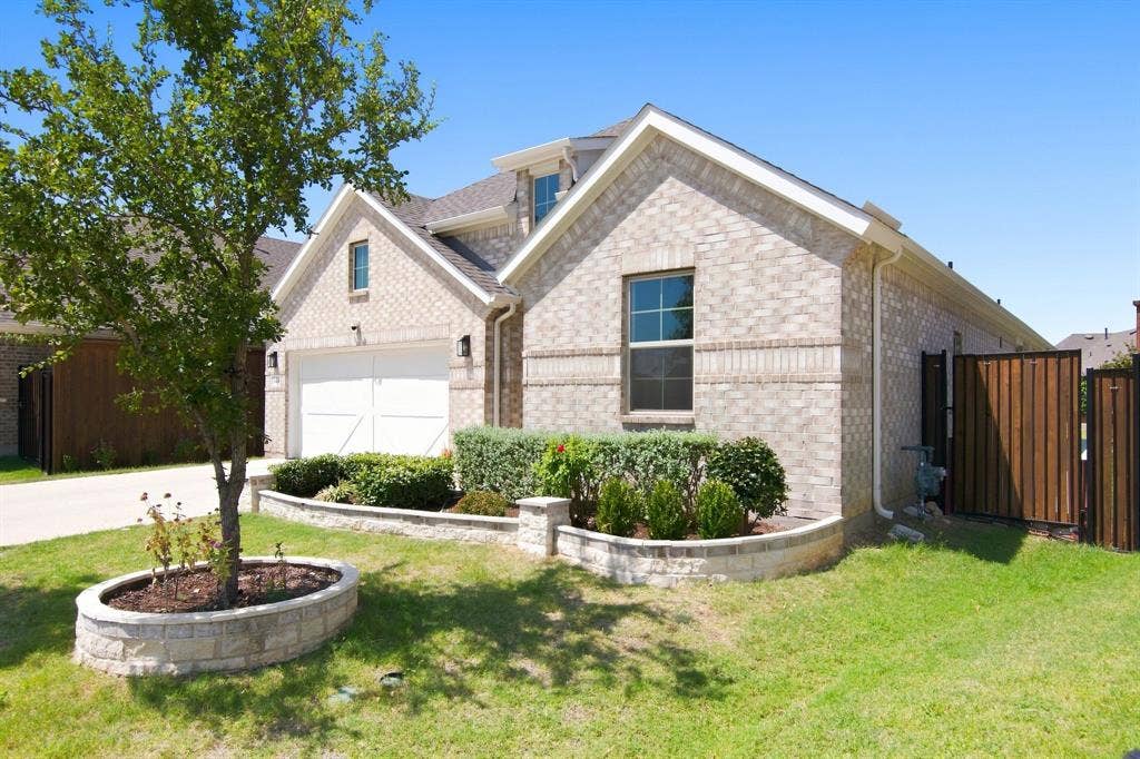 944 Tara Court, Haslet, TX 76052 Brick facade residence featuring a two-car garage, manicured landscaping in stone-edged beds, a privacy fence, and a mature tree