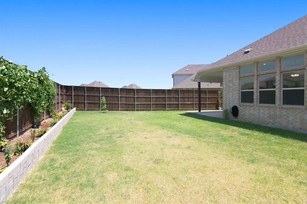 944 Tara Court, Haslet, TX 76052 Spacious backyard featuring a substantial lawn, perimeter privacy fencing, and a concrete retaining wall bordering a cultivated garden bed with established plantings