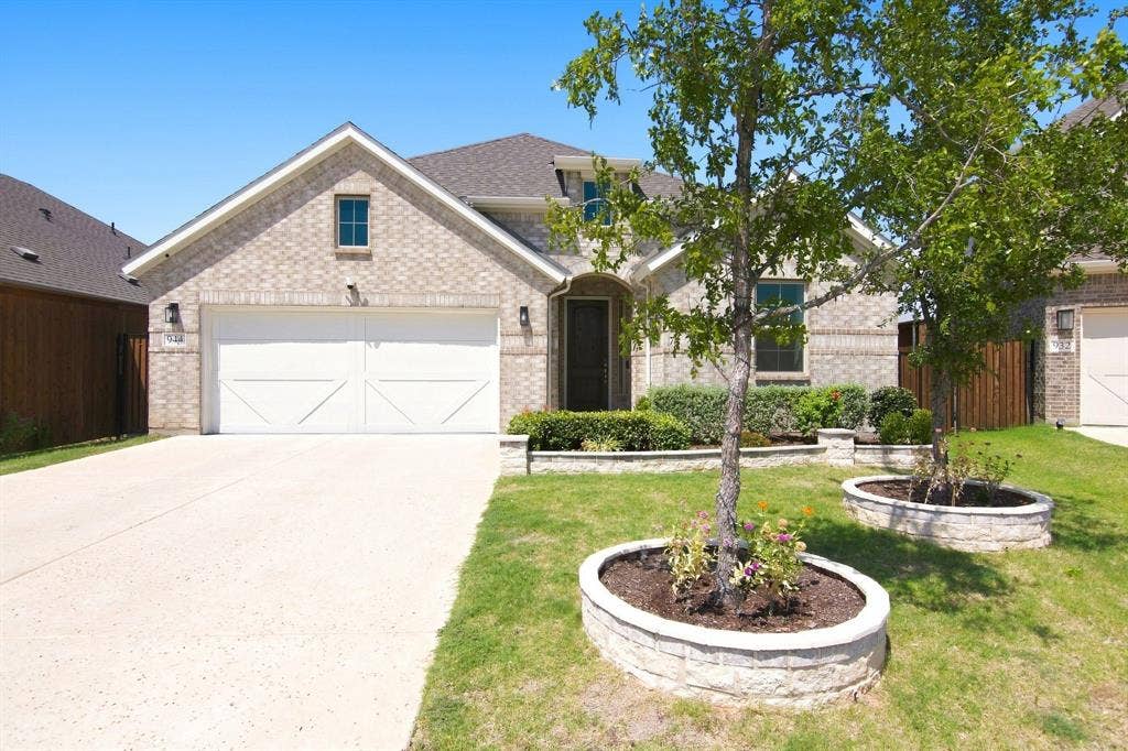 944 Tara Court, Haslet, TX 76052 Brick facade residence featuring a two-car garage with white paneled doors, an arched entry, a concrete driveway, and landscaped planting beds with stone retaining walls