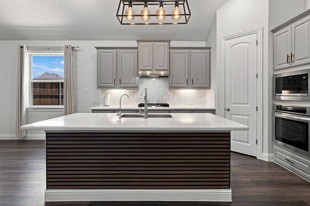 944 Tara Court, Haslet, TX 76052 Spacious kitchen featuring a large island with a slatted wood-finish base and light-toned countertop, gray cabinetry, built-in stainless steel appliances, a range hood, and wood-finish flooring