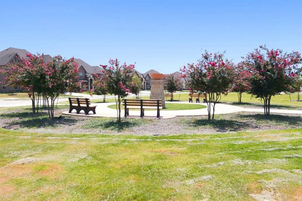 944 Tara Court, Haslet, TX 76052 Community green space featuring a circular walking path, multiple park benches, mature flowering trees, and a central stone monument