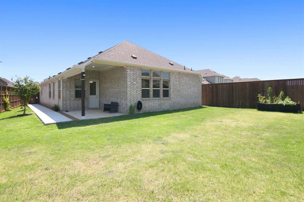 944 Tara Court, Haslet, TX 76052 Modern brick residence showcasing a spacious rear elevation with large multi-pane windows, a covered patio area, and a pitched roof with architectural detail