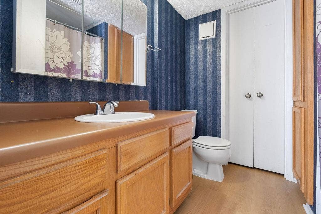 Bathroom featuring a wood-finish vanity with an integrated sink, a medicine cabinet, a toilet, and bifold closet doors