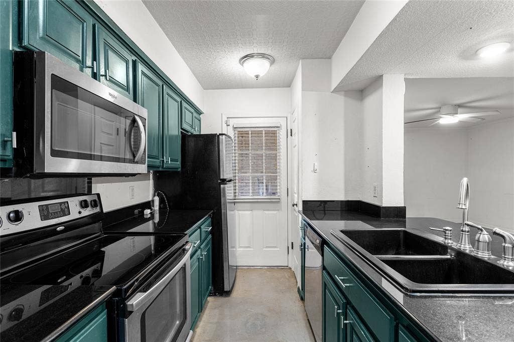 5916 Birchbrook Drive, #129, Dallas, TX 75206 Galley kitchen featuring teal cabinetry, black countertops, stainless steel appliances, and a double basin sink with a chrome faucet