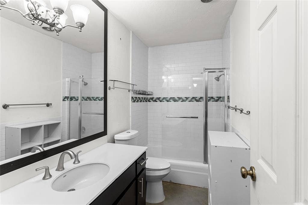 5916 Birchbrook Drive, #129, Dallas, TX 75206 Bathroom featuring a vanity with an integrated sink, a rectangular mirror, and a shower-tub combination with sliding glass doors