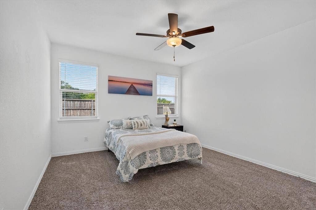 Carpeted room featuring a ceiling fan with integrated lighting, two windows with blinds, and white baseboards