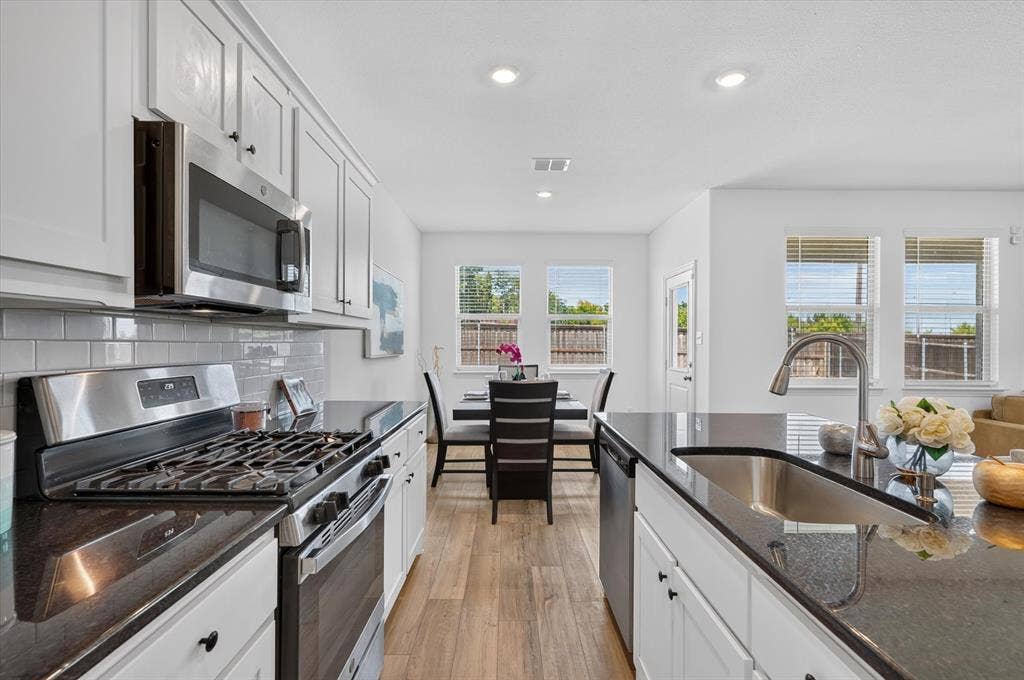 Chef's kitchen featuring white cabinetry, stainless steel appliances including a gas range and built-in microwave, dark quartz countertops, subway tile backsplash, and wood-finish flooring