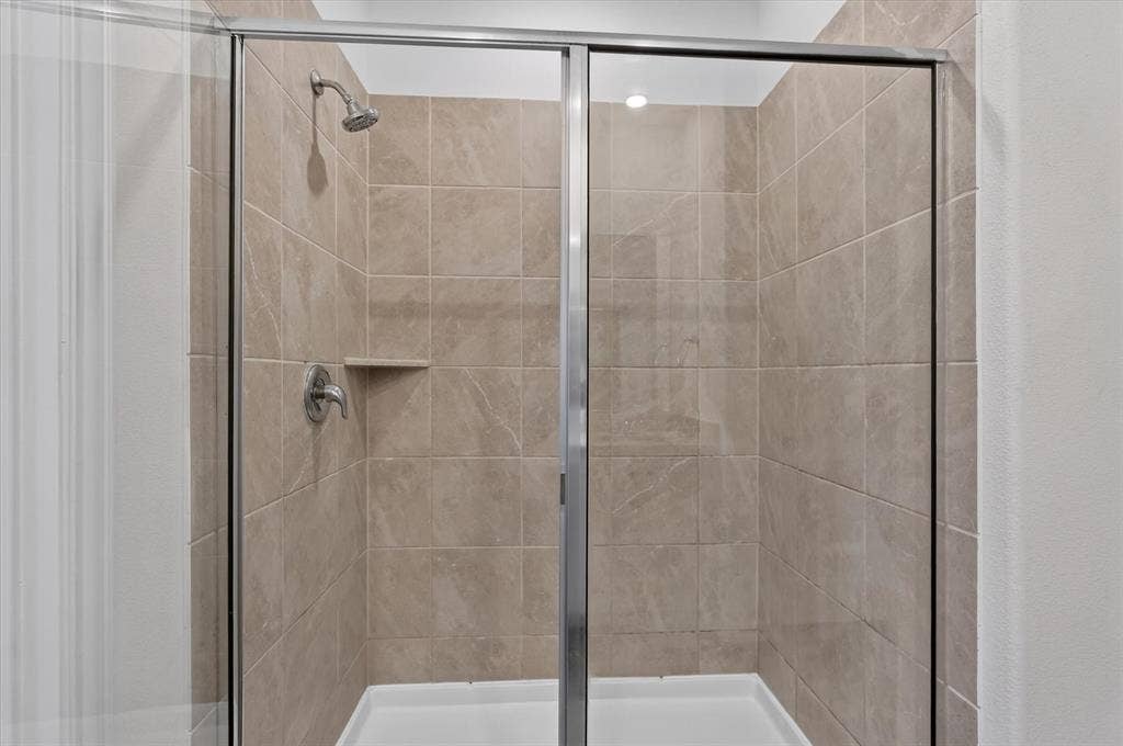 Spa-inspired shower enclosure featuring frameless glass doors with polished chrome hardware, neutral tile surround with linear layout, dual showerheads with individual controls, and a spacious walk-in configuration with built-in shelf niche
