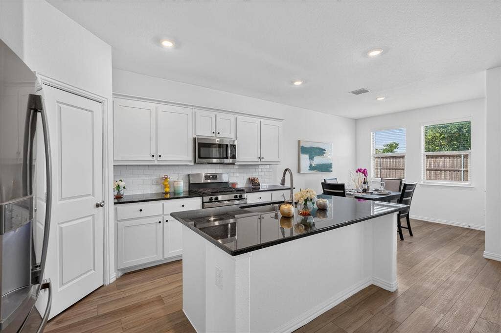 Bright kitchen featuring white cabinetry, dark countertops, white subway tile backsplash, stainless steel appliances, and wood-finish flooring