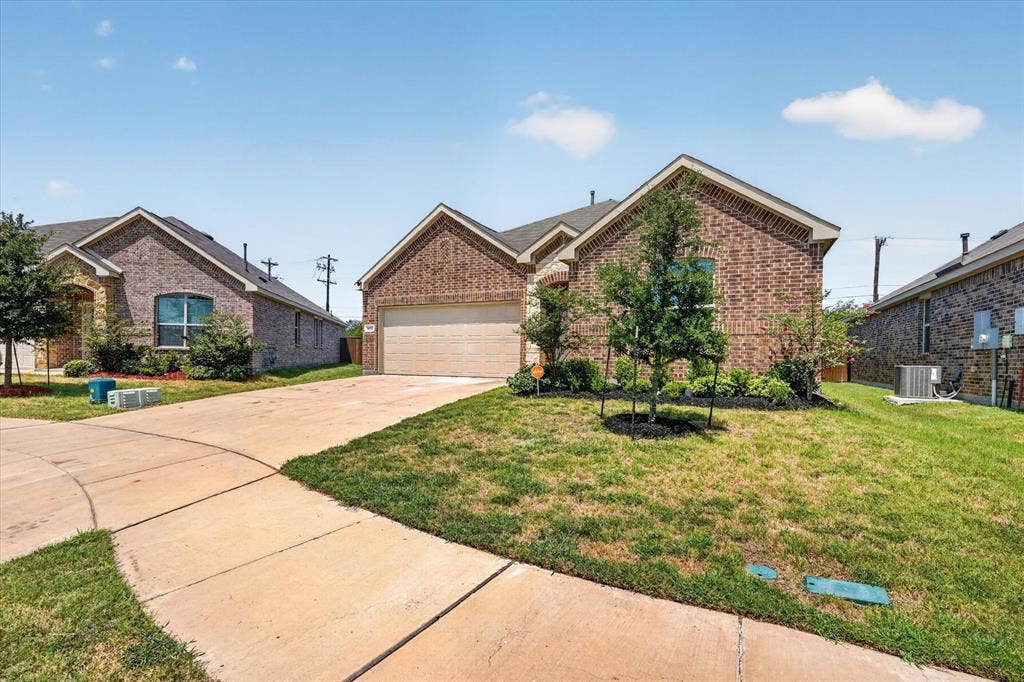 Charming brick home featuring a three-car garage, manicured front lawn with mature landscaping, and a wide concrete driveway