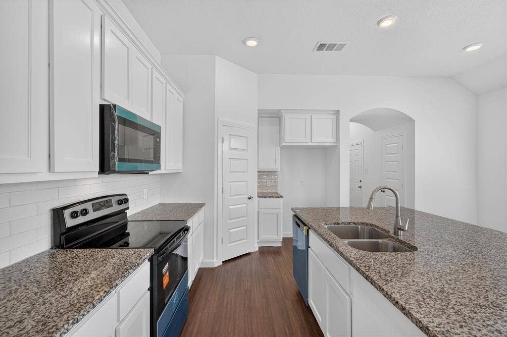 2832 Lolita Way, Forney, TX 75126 Galley-style kitchen featuring white cabinetry, granite countertops, stainless steel appliances including a gas range and microwave, dual undermount sinks with gooseneck faucet, and wood-finish flooring throughout