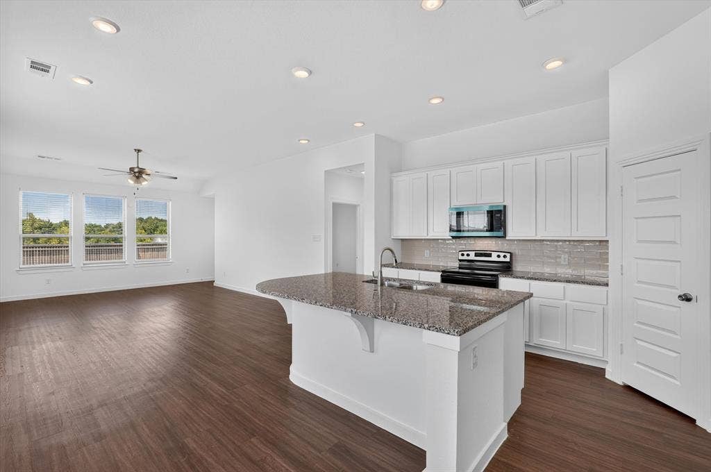 2832 Lolita Way, Forney, TX 75126 Open-concept kitchen and living area featuring a large island with granite countertop, stainless steel appliances, white cabinetry, and recessed lighting throughout