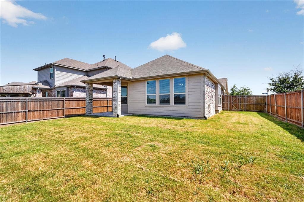 2832 Lolita Way, Forney, TX 75126 Expansive backyard featuring a covered patio with stone columns, a wood privacy fence, and multiple windows across the rear elevation