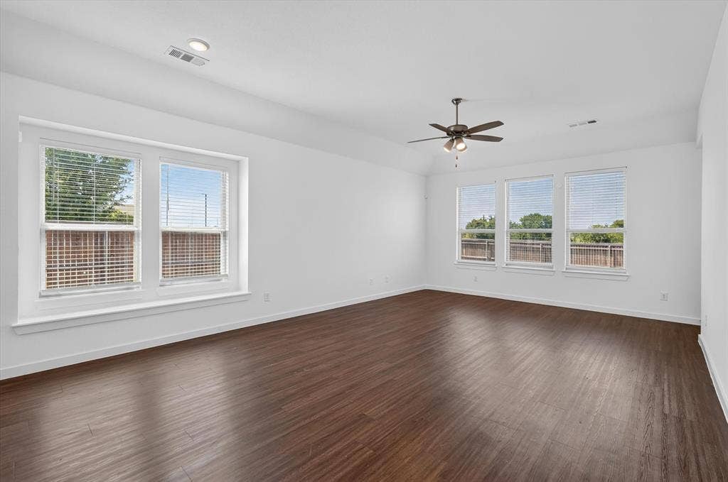2832 Lolita Way, Forney, TX 75126 Spacious room featuring gleaming wood-finish flooring, abundant natural light from dual window banks, ceiling fan with integrated lighting, and clean white walls with neutral trim throughout