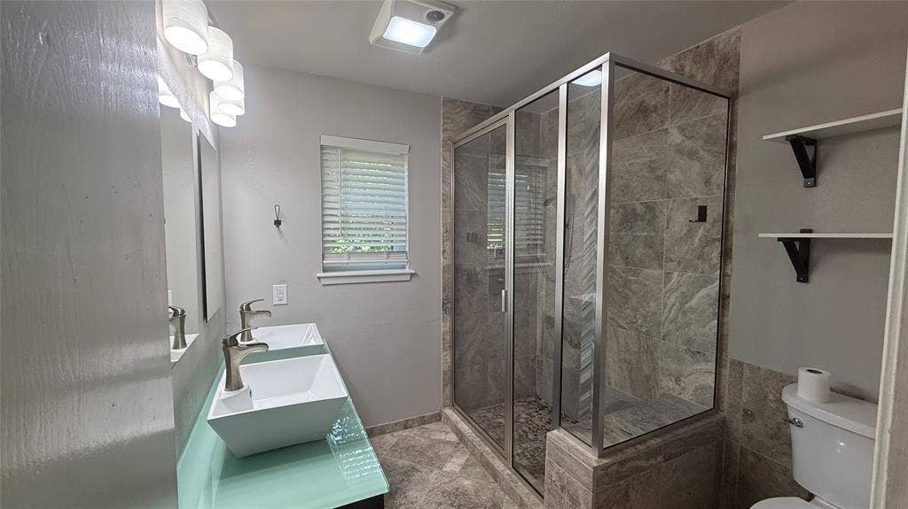 106 E Fairway Drive, Hideaway, TX 75771 Bathroom featuring a dual vanity with vessel sinks, a glass-enclosed shower with stone tile, and built-in shelving
