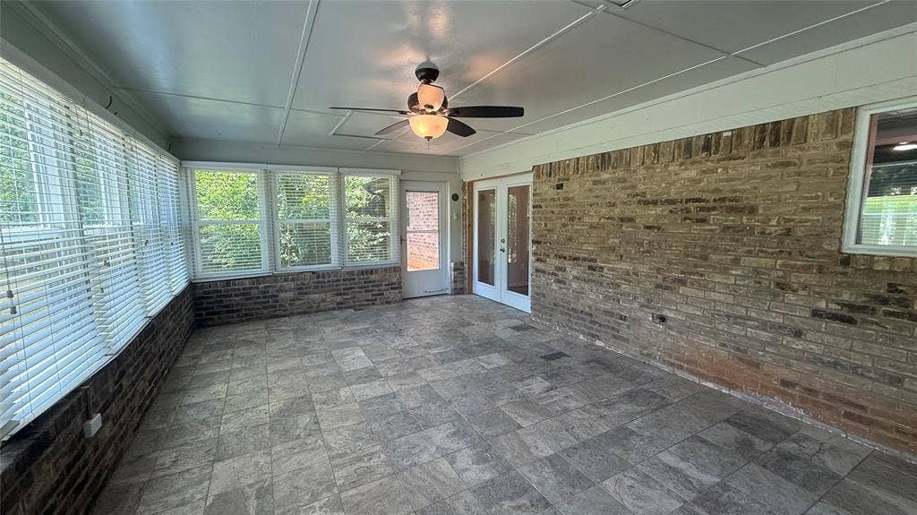 106 E Fairway Drive, Hideaway, TX 75771 Enclosed patio featuring tile flooring, a ceiling fan with light fixture, multiple windows with blinds, a brick accent wall, and double glass doors