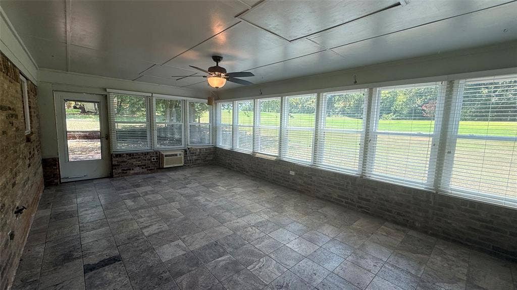 106 E Fairway Drive, Hideaway, TX 75771 Enclosed sunroom featuring extensive window-lined walls, a tiled floor, a ceiling fan with integrated lighting, and a brick half-wall
