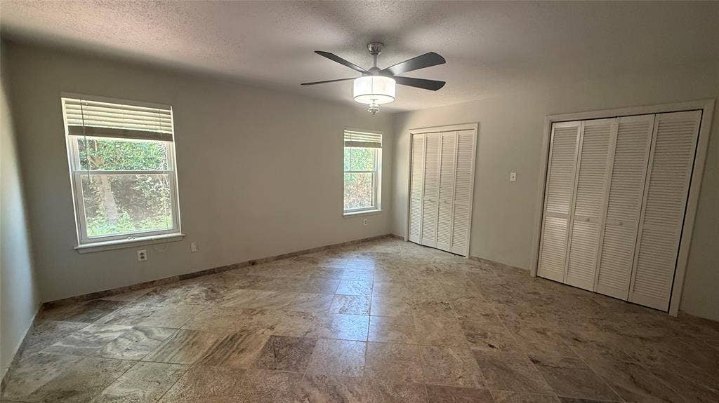 106 E Fairway Drive, Hideaway, TX 75771 Spacious room featuring large format tile flooring, two windows with blinds, a ceiling fan with integrated lighting, and two sets of bi-fold louvered closet doors