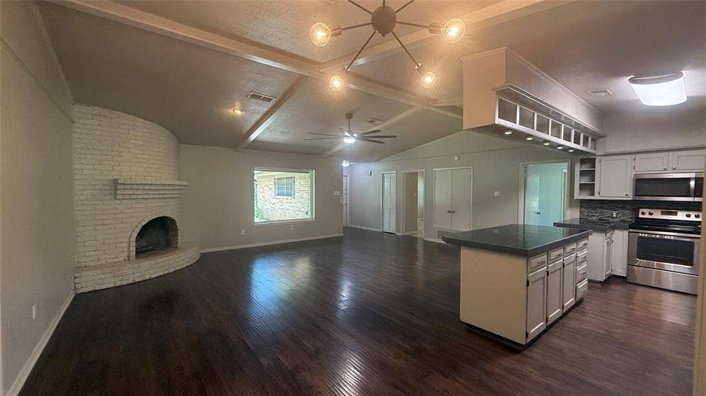 106 E Fairway Drive, Hideaway, TX 75771 Open-concept interior featuring wood-finish flooring, a white brick fireplace, vaulted ceilings with exposed beams, an island with a dark countertop, and stainless steel kitchen appliances