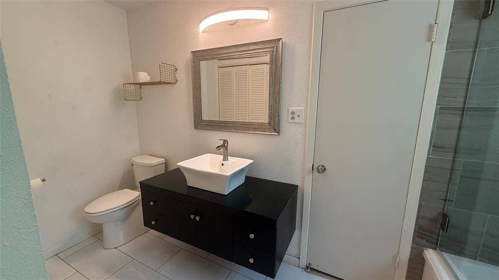106 E Fairway Drive, Hideaway, TX 75771 Contemporary bathroom featuring a floating black vanity with a vessel sink, a framed mirror, and light-toned tile flooring