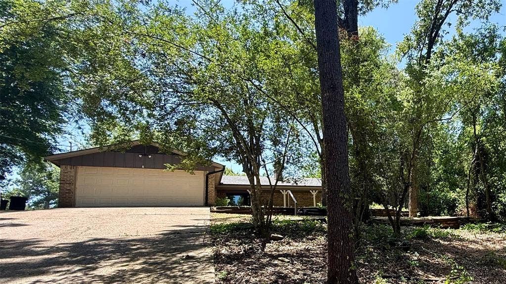 106 E Fairway Drive, Hideaway, TX 75771 Brick and siding exterior featuring a multi-car garage, pitched roofline, and an expansive gravel driveway