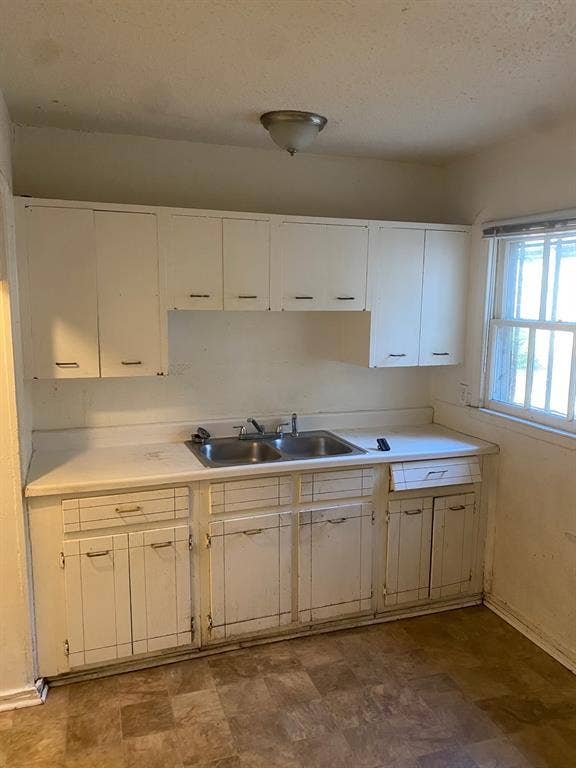 Kitchen featuring white cabinetry, a double basin stainless steel sink, a window, and resilient sheet flooring
